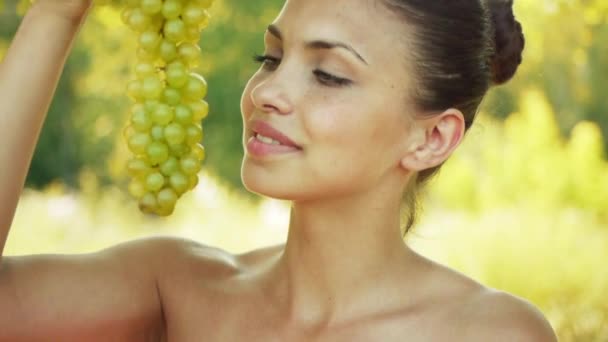 Beautiful young woman bites off from grape bunches, against summer green park. — Stock Video