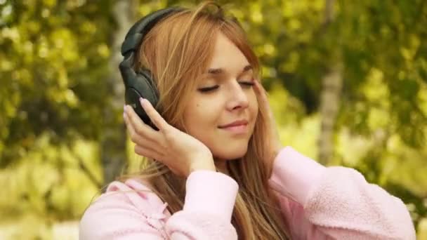 Close-up portrait of young pensive woman listening to music at summer green park. — Stock Video