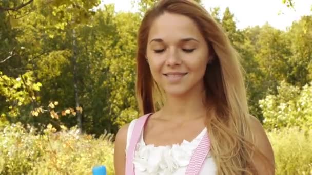Portret van jonge mooie vrouw met blote schouders drinkt uit fles van koud water, op groene achtergrond zomer aard. — Stockvideo