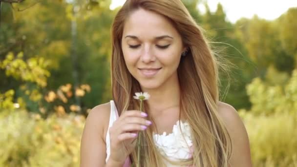 Portrét mladé krásné ženy diví, trhání okvětních lístků na sedmikrásky na zeleném pozadí letní přírody. — Stock video