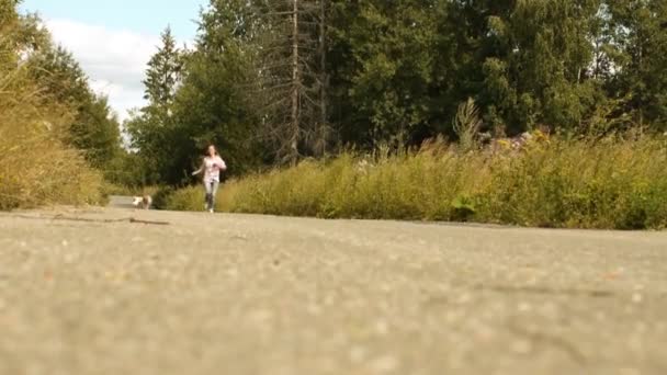 Giovane bella donna capelli lunghi vestito corto corre su strada forestale con guinzaglio cane — Video Stock