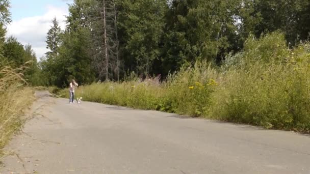 Молодая красивая женщина длинные волосы короткое платье работает на лесной дороге с собачьим поводком — стоковое видео