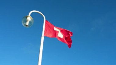 İsviçre bayrağı mavi gökyüzünün arka planında bir lamba ile bir bayrak direği üzerinde uçan.