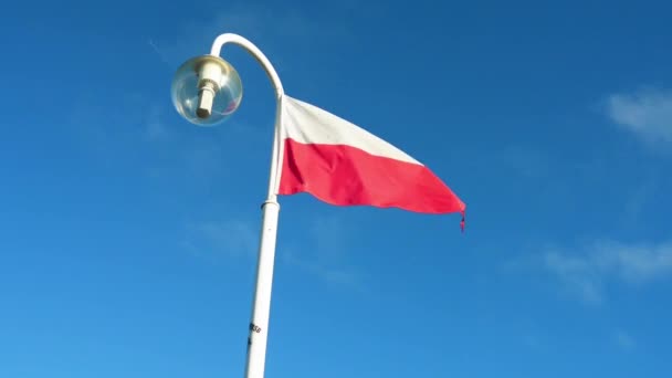 La bandera de Polonia ondeando sobre un asta de la bandera con una lámpara sobre un fondo de cielo azul . — Vídeo de stock