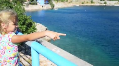 Küçük gülümseyen güzel kız Hırvatistan Adriyatik kıyısındaki korkuluk yakınındaki ayakta.