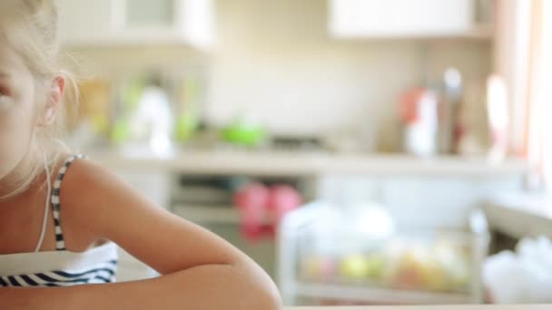 Hermosa niña rubia bebiendo jugo en la mesa de la cocina . — Vídeos de Stock