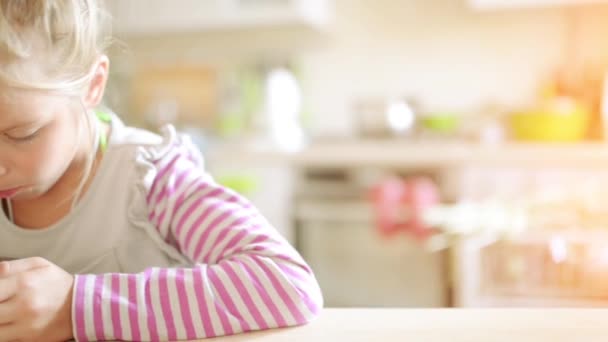 Hermosa niña rubia comiendo cereal en la mesa de la cocina . — Vídeos de Stock