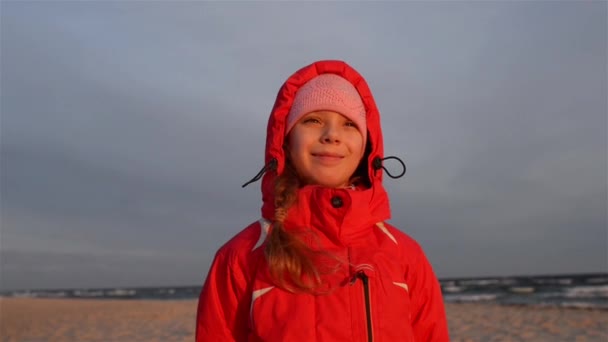 Hermosa adolescente sonriente con una chaqueta roja sobre un fondo de una costa báltica de invierno . — Vídeos de Stock