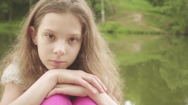 少し悲しい少女は湖の近くの木造の橋に座っている美しい. — ストック動画