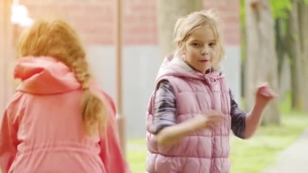 Dvě holčičky si hrají s koulí v jarním zeleným městském parku. — Stock video