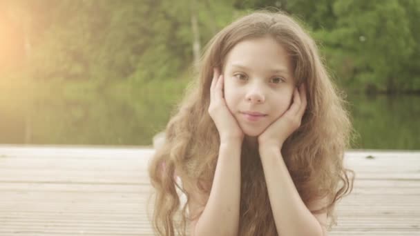 Bella bambina è sdraiata sul ponte di legno vicino al lago . — Video Stock