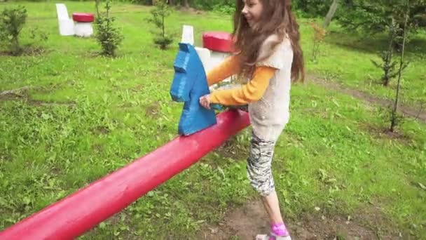 Menina bonita montando em um balanço no parque da cidade de verão . — Vídeo de Stock