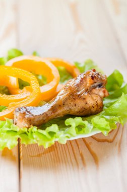 Kızarmış iştah açıcı tavuk inciği ve doğranmış halkalar. Sarı biber, ahşap bir masada yeşil bir salatanın üzerinde yatar..