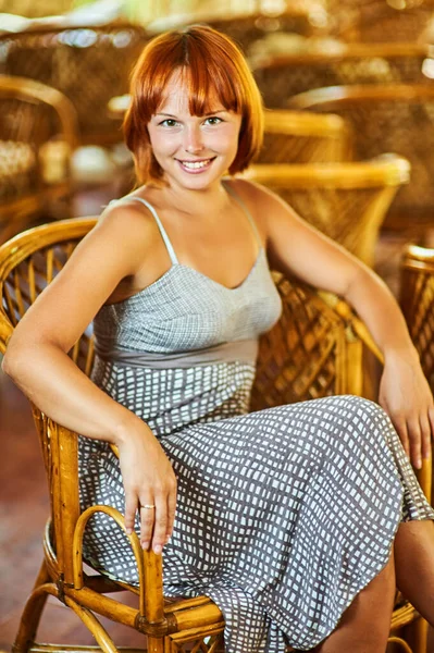 若いです美しいです女性で遊んだドレスに座っている木製のウィッカーチェアと笑顔 — ストック写真
