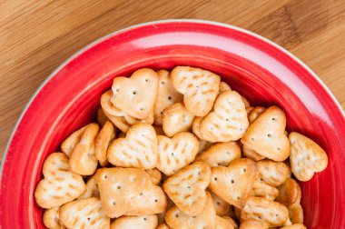 Tahta bir masada kırmızı bir kasede kupa şeklinde sarı kuru kraker..