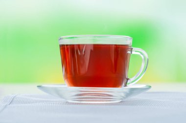 Yeşil arka planda bir fincan üzerinde siyah çay ile şeffaf bardak.