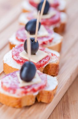 Sosisli sandviç, peynir ve zeytinli kürdan, arka planda ahşap masa..