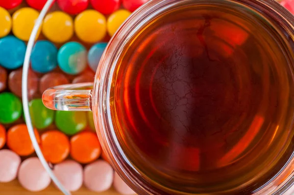 在多种颜色的糖果中 有圆形玻璃杯 透明的 茶托和一杯 放在厨房木制餐桌的后面 — 图库照片