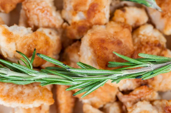 Fried chicken pieces with rosemary in a plate on wooden table.