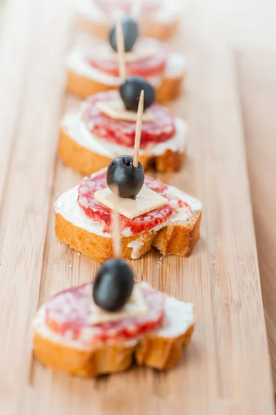 ソーセージサンドイッチ チーズとオリーブのつまようじ 背景に木製のテーブル — ストック写真