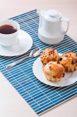 Tabakta küçük kekler, bir sürahi süt ve mavi bambu masa örtüsünde bir fincan çay..