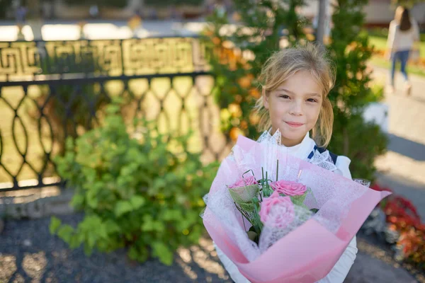 Piękna Dziewczynka Trzyma Rękach Duży Bukiet Kwiatów Pobliżu Ogrodzenia Szkolnego — Zdjęcie stockowe