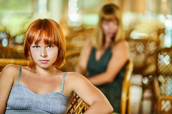 二人の若い悲しい女性はウィッカーチェア付きの大きな部屋の背景に互いに動揺 — ストック写真