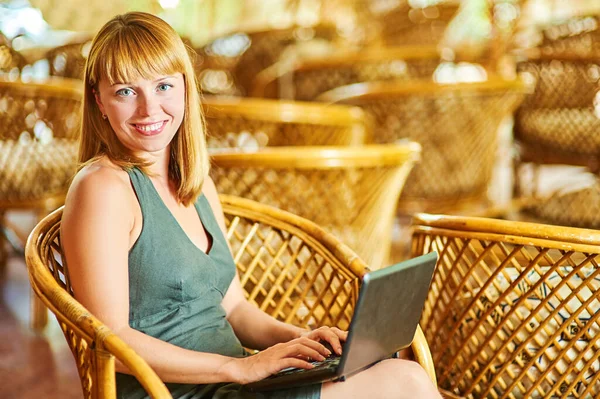 穿着绿色衣服的年轻漂亮的女人坐在木制柳条椅上 在黑色笔记本电脑上工作 — 图库照片