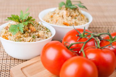 Bambu masa örtüsü üzerinde kırmızı domates. Arka planda maydanozla süslenmiş et ve pirinçli pilav..