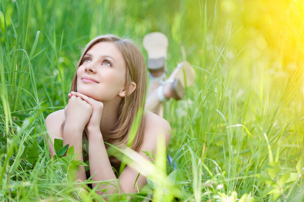 Молодая красивая улыбающаяся женщина лежит на зеленой траве и смотрит вверх на фоне летнего городского парка.