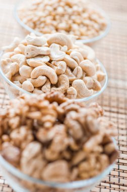 Cevizli üç cam kase, beyaz susam tohumu ve bambu peçetede kaju fıstığı..