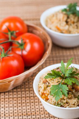 Et ve pirinçle süslenmiş, bambu masa örtüsünde maydanozla süslenmiş. Arka planda kırmızı domatesler.