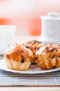 Tabakta küçük kekler, bir sürahi süt ve mavi bambu masa örtüsünde bir fincan çay..