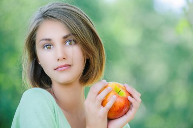 Yeşil bluzlu güzel, sakin bir kadın yaz parkında elinde büyük kırmızı bir elma tutuyor..