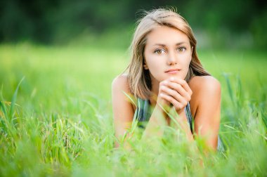 Genç ve sakin bir kadın yeşil çimlerin üzerinde yatıyor..