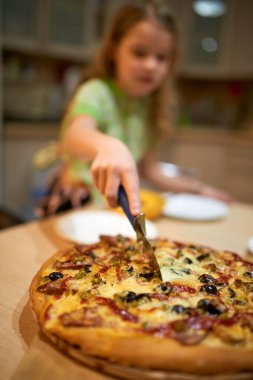 Mutfakta elinde pizza keskisiyle ev kıyafetleri içinde küçük bir kız..