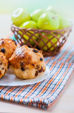 Kuru üzümlü kekler masa örtüsünün üzerinde bir tabakta yatıyor. Yakınlarda elmalı bir sepet var..