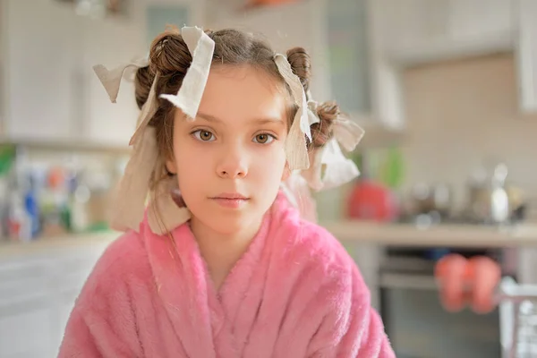 彼女の髪にリボンと暖かいピンクのローブのかなり小さな女の子は台所でカメラを見ている — ストック写真