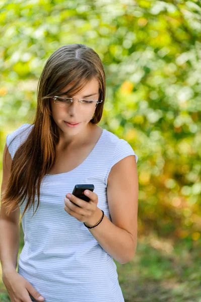 一个戴着眼镜 留着长发的年轻美丽的微笑的女人正在以夏日绿色的背景阅读短信 — 图库照片
