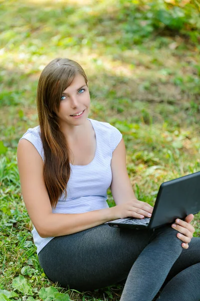 Młoda Słodka Uśmiechnięta Kobieta Siedzi Zielonej Trawie Trzyma Czarny Laptop — Zdjęcie stockowe