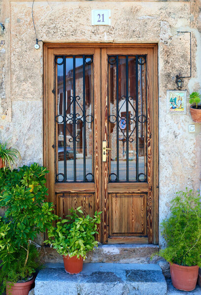 Beautiful elegant wooden door with glass exhibitions and metal grille. Pots with flowers stand on the threshold at home. Old stone house.