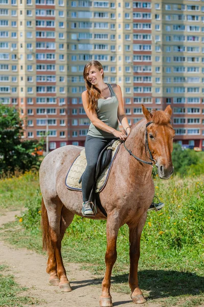 多階建ての家の近くの夏のダウンタウンの茶色の馬の上の美しい若い女性 — ストック写真