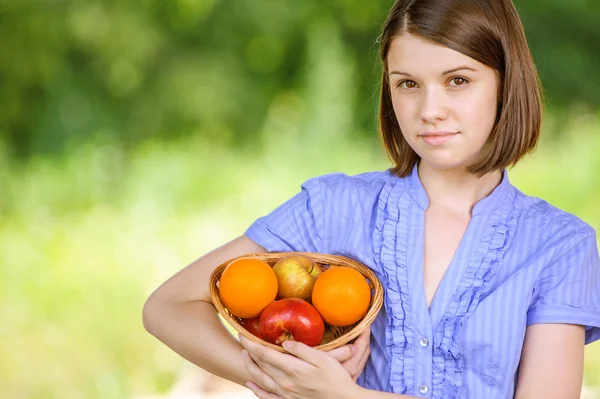 Portrait of young smiling brunette holding basket with fruits — Stock Photo, Image