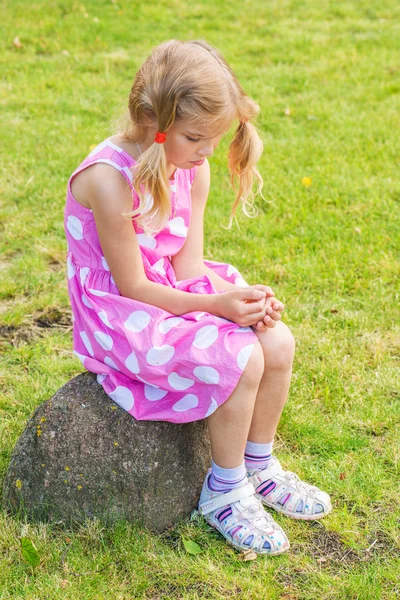 Little sad girl sitting on stone — Stock Photo, Image