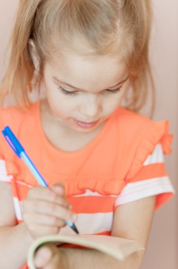 küçük kız kalem not defterinde yazıyor.