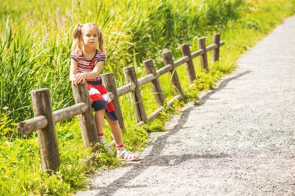 Little sad girl sitting on wooden fence — Stock Photo, Image