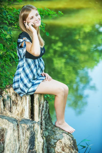Porträt einer jungen Frau, die auf einem Baumstumpf sitzt und am Handy spricht — Stockfoto