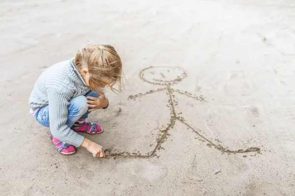 Little girl sand draws funny man — Stock Photo, Image
