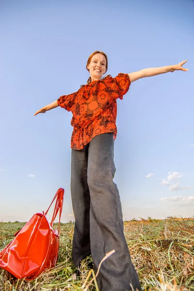 Woman with red bag standing in field — Stock Photo, Image