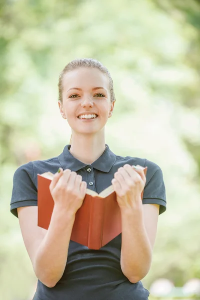 Sorrindo jovem mulher em blusa escura lê livro vermelho — Fotografia de Stock